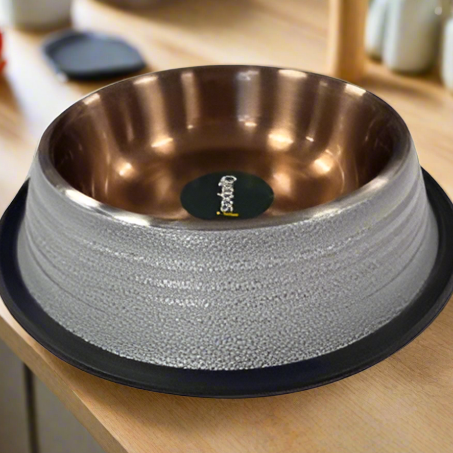 A white, ribbed non-slip bowl with a copper interior, placed on a black mat, with a branded label in the center.