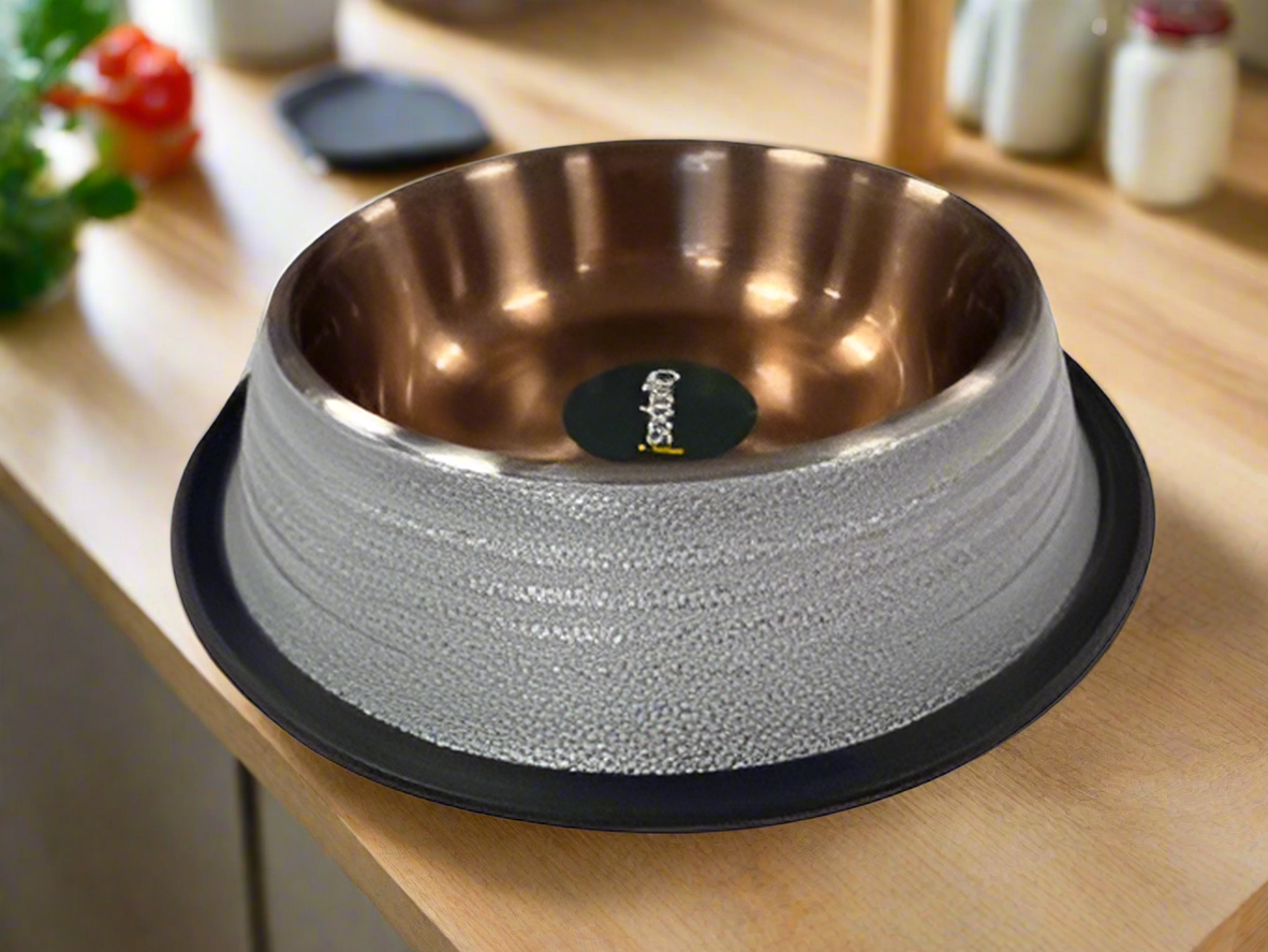 A white, ribbed non-slip bowl with a copper interior, placed on a black mat, with a branded label in the center.