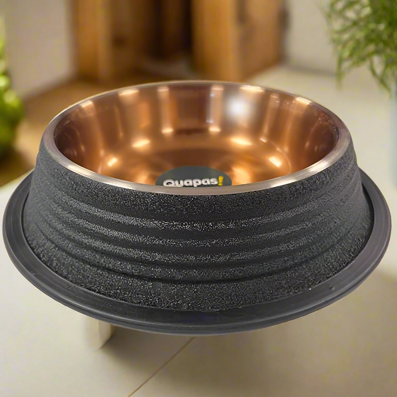 A black, ribbed, non-skid bowl with a copper-colored interior, placed on a table with a plant in the background.