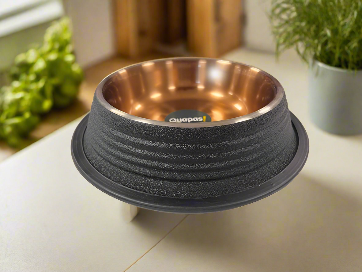 A black, ribbed, non-skid bowl with a copper-colored interior, placed on a table with a plant in the background.