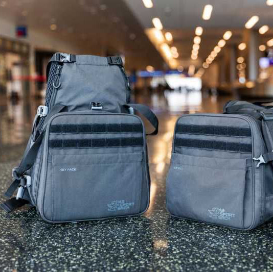 Two gray bags with straps on a reflective surface in an indoor setting